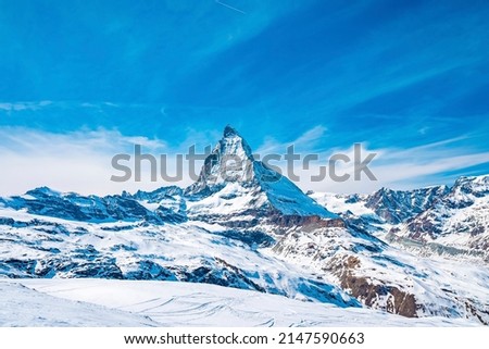 Scenic view of snowcapped matterhorn mountain peak. Famous snow covered white landscape against blue sky. Beautiful snowy valley in alps during winter. Royalty-Free Stock Photo #2147590663