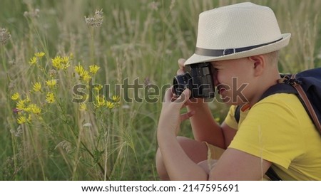 Happy boy, child dreams of becoming photographer. Concept of children's fantasy in nature. Child boy plays with camera, photography flowers in summer park. Child dreams of traveling making discoveries