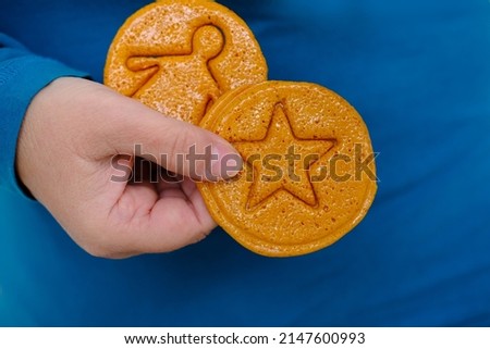 closeup female hand holding round yellow caramel sugar cookies with embossed star for popular Korean children's game, cut out figure with needle, do not crumble pattern, holiday homemade food