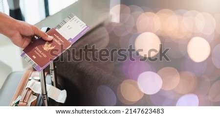 Close up hands the man going to flight with suitcase holding Thailand passport and airline ticket on baggage luggage of tourist in airport while waiting for boarding time departure on holiday, travel Royalty-Free Stock Photo #2147623483