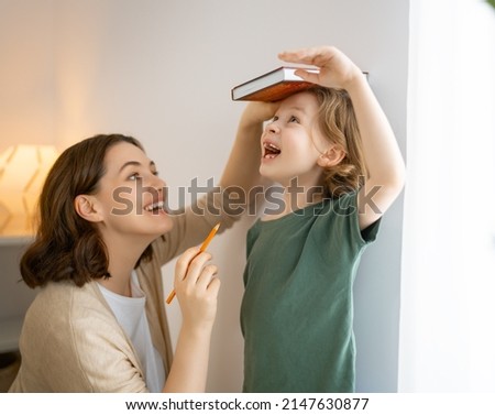Kid and mother are measuring the growth on the background of wall. Happy family at home.  Royalty-Free Stock Photo #2147630877