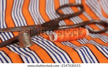 Spool of Orange Thread and Thimble on Orange and White Striped Fabric