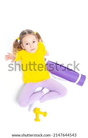 Little cute happy girl lies with dumbbells and gymnastic mat. Isolated on white background. View from above
