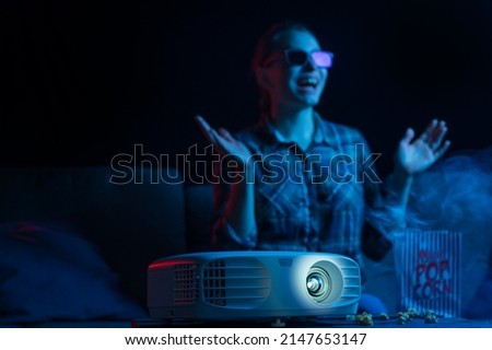 Girl watching a movie. Watching movies in 3D, with glasses. Cinema for home, relaxation and fun. Popcorn. Creative light.
