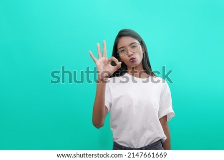 Photo of cheerful young indian asian woman, makes okay gesture with both hands, demonstrates her agreement, feels happy, wears casual outfit, isolated over blue background.