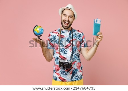 Cheerful young traveler tourist man in summer clothes hat photo camera hold Earth world globe passport tickets isolated on pink background. Passenger traveling on weekend. Air flight journey concept