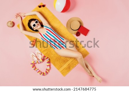 Top view full body satisfied young woman of Asian ethnicity in striped swimsuit sunglasses lies on towel hotel pool isolated on plain pastel pink background. Summer vacation sea rest sun tan concept