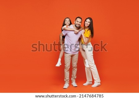 Full size young fun happy parents mom dad with child kid daughter teen girl in basic t-shirts giving piggyback to daughter isolated on yellow background studio Family day parenthood childhood concept. Royalty-Free Stock Photo #2147684785