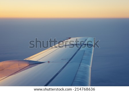 Wing of an airplane flying above the clouds at the sunrise