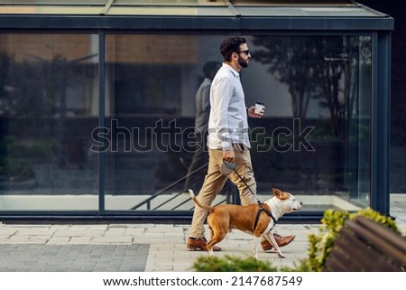 A businessman dressed in a white shirt holding coffee to go and walking his dog. A businessman on a lunch break with his dog Royalty-Free Stock Photo #2147687549