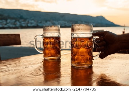 Cold beer in the hands, toast with a mug of beer on the coast in the sunset. Summer, Party, Holiday,	