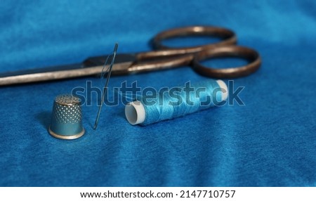 Spool of Blue Thread, Thimble and Needle on Blue Fabric