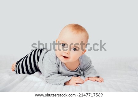 Seven month old baby child sitting on bed. Cute smiling little infant girl on white soft blanket. Charming blue eyed baby. Copy space. Royalty-Free Stock Photo #2147717569