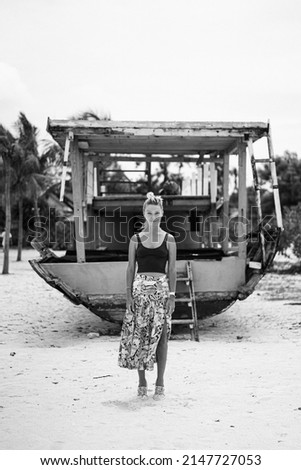 Young woman traveling on the beach against the backdrop of an old ship.