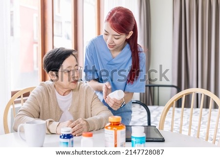 Asian mature senior woman holding a medical bottle and asking for information from the nurse before administering medication. Caregiver visit at home. Home health care and nursing home concept.