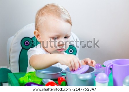 A little girl plays with toy vegetables on the background of children's dishes.