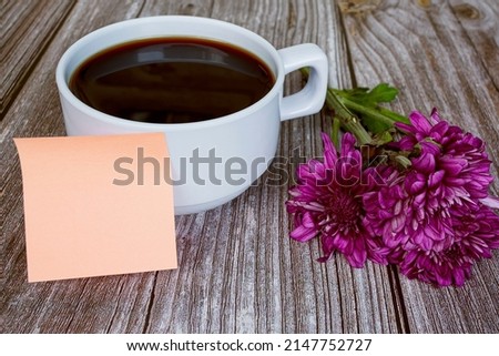 Sticky note with white coffee cup and flowers on wooden desk. Copy space.