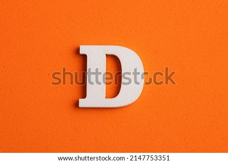 Alphabet letter D - White wood piece on orange foamy background