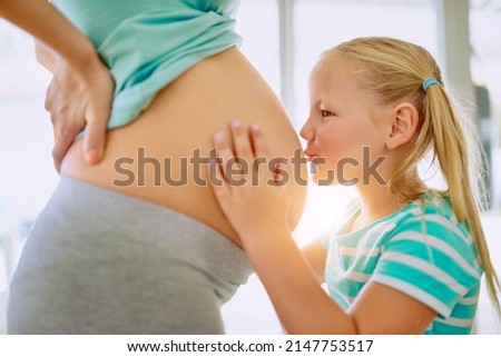 Were going to have so much fun, little baby. Shot of a little girl kissing her mothers pregnant belly at home.