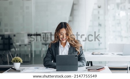 A businesswoman is checking company financial documents and using a tablet to talk to the chief financial officer through a messaging program. Concept of company financial management. Royalty-Free Stock Photo #2147755549