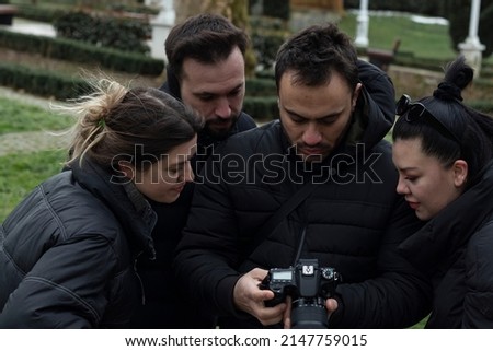 Four friends looking photographs in camera. Outside, park background.