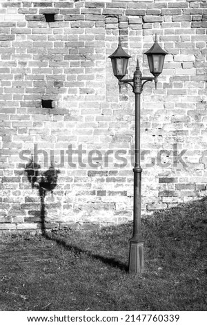 An old street lamp that casts a shadow over a brick wall. Black and white picture.