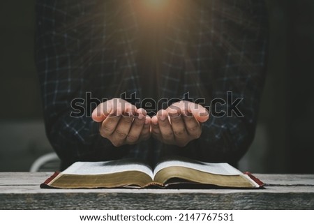 Man hands praying to god with the bible. Yellow lights and sparkles coming on Believe in goodness. Holding hands in prayer on a wooden table. Power of hope or love and devotion.  Royalty-Free Stock Photo #2147767531
