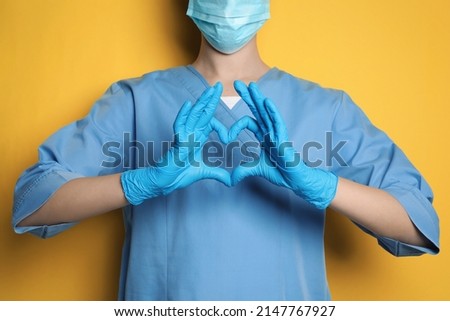 Doctor making heart with hands on yellow background, closeup