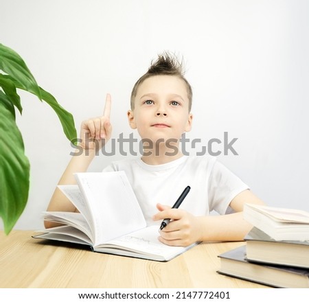 The boy writes in a notebook and looks up thoughtfully. copy space