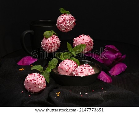 Pink round biscuit muffins sprinkled with icing lying on a black surface with a reflection on a black background with mint leaves.