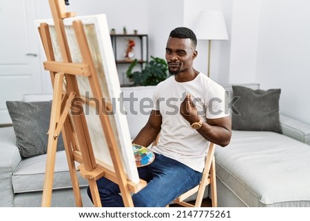 Young african man painting on canvas at home doing money gesture with hands, asking for salary payment, millionaire business 