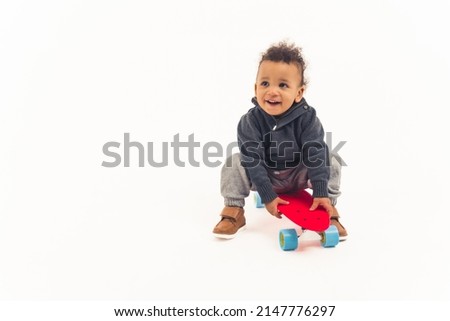 Biracial baby's first skateboard ride. Curious toddler sitting on a red skateboard over white background. High quality photo