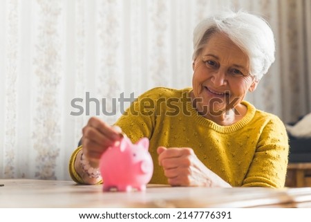 let's save money - nice senior woman putting a coin in piggy bank medium closeup room savings concept. High quality photo