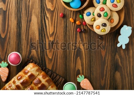 Easter hot cross buns with colored eggs Easter gingerbread rabbits and cookies over dark brown plank wooden old table background. Spring holiday baking concept. Easter table setting. Top view. Mock up