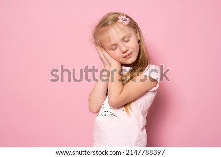 Relax and sleep time. Tired Cute Caucasian kid girl standing isolated over pink background with closed eyes leaning on palms making sleeping gesture.