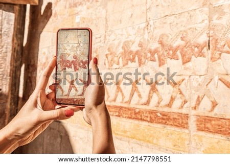 Travel blogger girl takes pictures on a smartphone at the famous Hatshepsut temple frescoes in the ancient city of Luxor in Egypt. Or using visual tourist guide