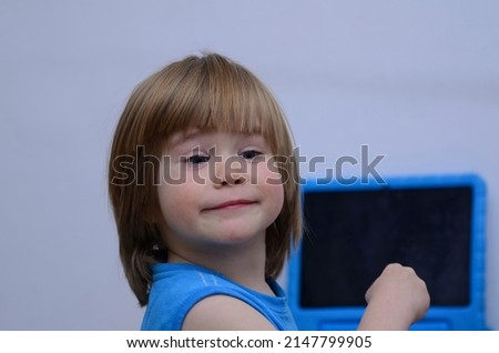 Little boy three years old. with long hair. Sitting at the table by the blue tablet - the child's emotions on content. The kid laughs. Tablet in a child's protective case.
