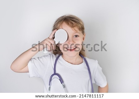 a little girl doctor smiles with a stethoscope and a eye flap, vision check. white background. health check concept. close-up