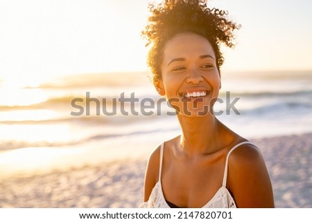 Smiling young black woman in beachwear enjoy sunset at beach. Satisfied beautiful girl with afro hair relaxing at beach during sunrise with copy space. African american woman daydreaming. Royalty-Free Stock Photo #2147820701