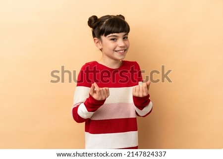 Little caucasian girl isolated on beige background making money gesture