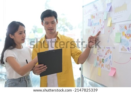Young asian woman and her colleague giving presenting new marketing strategy on flip chart.