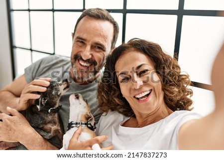 Middle age hispanic couple smiling happy making selfie by the camera. Lying on the bed with dogs at home.