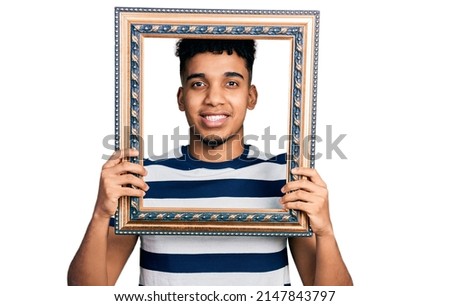 Young african american man holding empty frame smiling with a happy and cool smile on face. showing teeth. 
