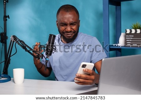 Portrait of influencer crying after reading on smartphone insulting comments from online social media account . Vlogger sitting at desk in vlogging studio deeply hurt by online bully.