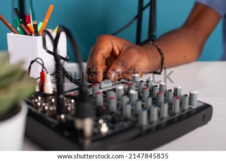 Closeup of content creator hand adjusting master volume fader on mixer console on desk during live podcast. Vlogger working on sound settings of equilizer used to broadcast live stream.