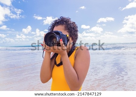 Woman on the beach on vacation photographing in summer. Young woman using camera at the beach