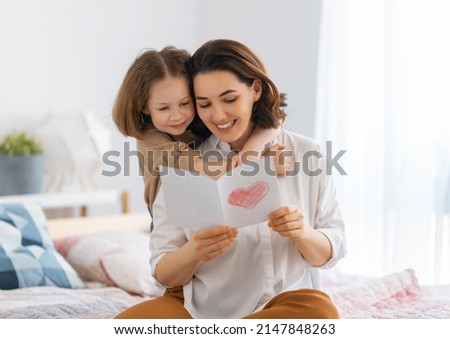 Happy mother's day. Child daughter is congratulating mom and giving her postcard. Mum and girl smiling and hugging. Family holiday and togetherness.