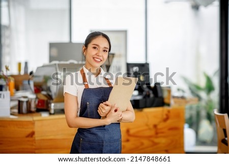 Opening a small business, AHappy Asian woman in an apron standing  near a bar counter coffee shop, Small business owner, restaurant, barista, cafe, Online, SME, entrepreneur, and  seller concept Royalty-Free Stock Photo #2147848661