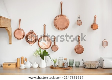 Different kind of cookware and ceramic plates on tabletop wooden kitchen. Set of copper saucepans, pans, pots and ladle hanging in kitchen. Hanging kitchen utensil on wall. kitchen interior decor
 Royalty-Free Stock Photo #2147859397