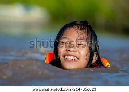 Children playing and swimming in river for relaxing time on summer season and holiday, close up girl kids smile and playful in water, child wearing life jacket for safety of activity outdoors 